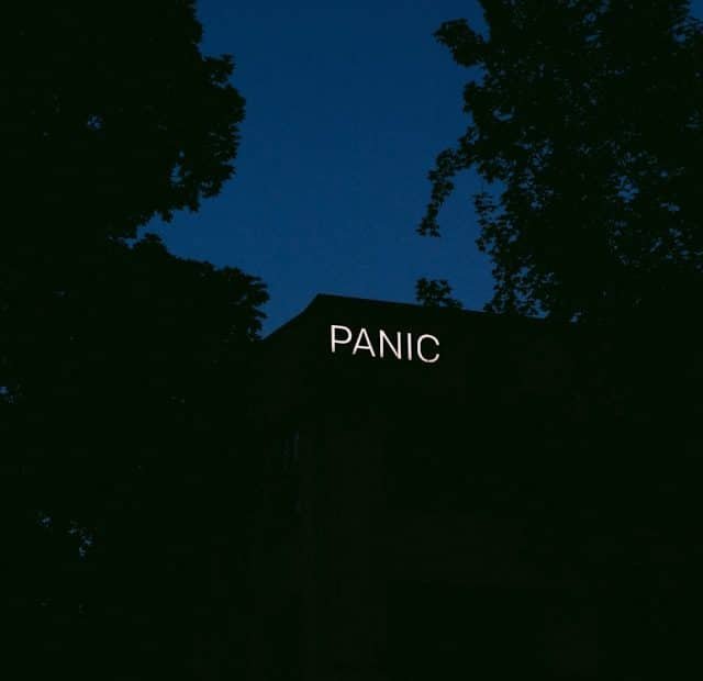 • LabNews AI Nighttime scene of a dark building with an illuminated PANIC sign on the roof framed by silhouetted trees against a blue sky